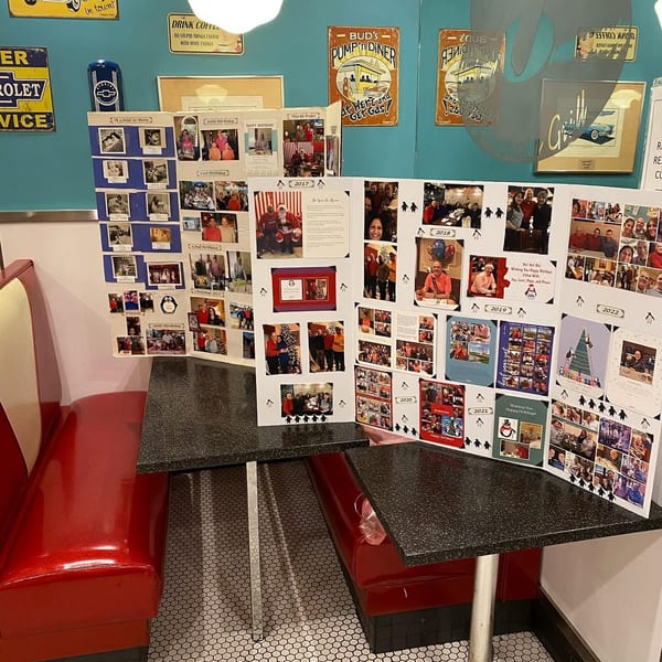 A diner booth with red seating and a table covered in a tri-fold display of family photos.