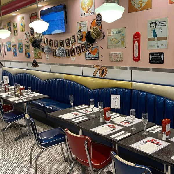 A retro diner interior with blue booths, black tables set with champagne flutes, and vintage decor.
