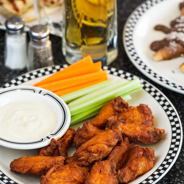 A plate of crispy chicken wings with ranch, celery, and carrots, alongside a beer and other dishes.